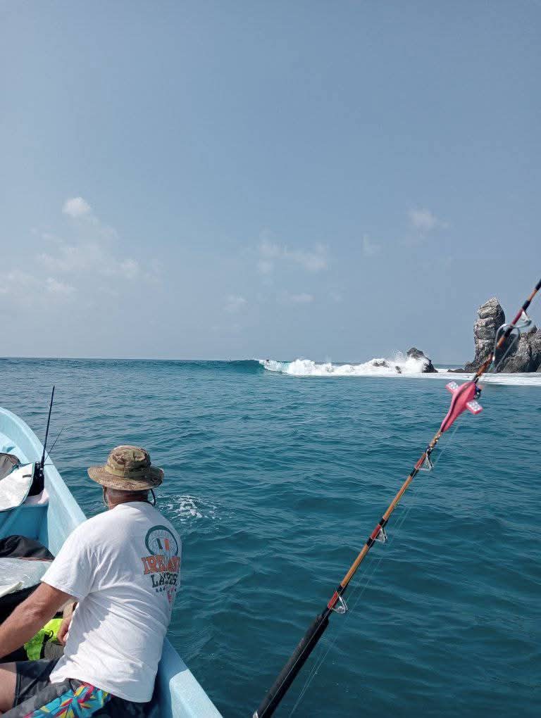 Surfer on a fishing boat with rods and a breaking wave in Salina Cruz, Oaxaca